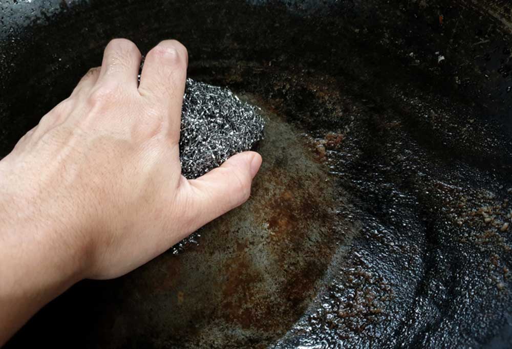 Person using steel wool to scrub burnt on grease from a flat grill top