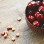 a bowl of cherries sitting on a wooden surface with cherry pits laying on a wooden surface