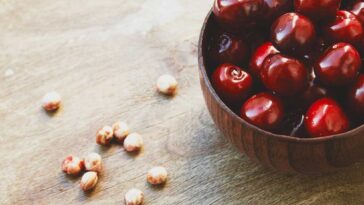a bowl of cherries sitting on a wooden surface with cherry pits laying on a wooden surface