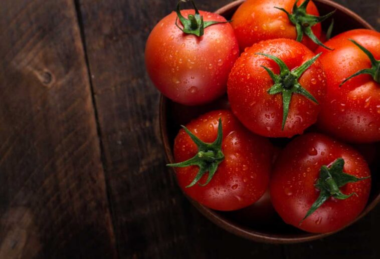 Bunch of tomatoes with stems in a bowl on a wooden table