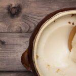 solid bacon grease in a stoneware pot with a wooden spoon in it