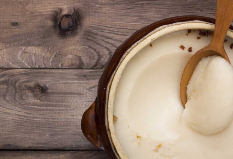 solid bacon grease in a stoneware pot with a wooden spoon in it