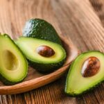 Avocado halves on a wooden table with and without the pits