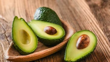Avocado halves on a wooden table with and without the pits