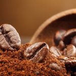 Coffee groumds and coffee beans in a wooden bowl spilling out onto a table.