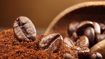 Coffee groumds and coffee beans in a wooden bowl spilling out onto a table.