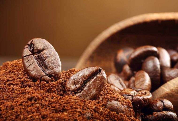 Coffee groumds and coffee beans in a wooden bowl spilling out onto a table.