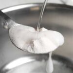 Vinegar being poured over a spoon of baking soda over a sink