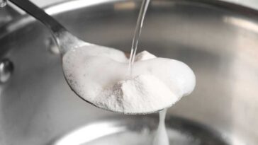Vinegar being poured over a spoon of baking soda over a sink