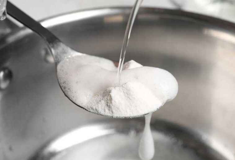 Vinegar being poured over a spoon of baking soda over a sink