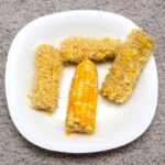 empty corn cobs with one whole ear of corn in the middle all on a white plate