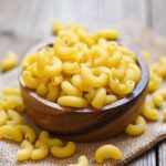 Uncooked macaroni noodles in a wooden bowl on a wooden table