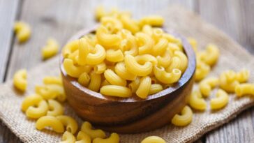Uncooked macaroni noodles in a wooden bowl on a wooden table