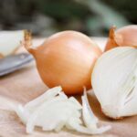Whole and cut onions with a knife on a cutting board