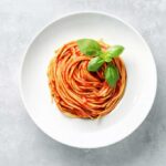Spaghetti plated in a spiral on a white plate with a basil garnish