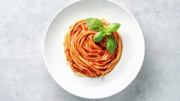 Spaghetti plated in a spiral on a white plate with a basil garnish