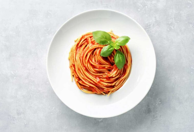Spaghetti plated in a spiral on a white plate with a basil garnish