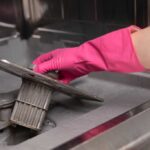 Hand wearing a pink glove, removing the filter from a dishwasher