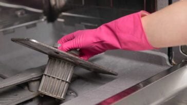 Hand wearing a pink glove, removing the filter from a dishwasher