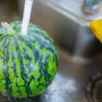 Small whole watermelon in a kitchen sink with water running on it