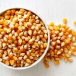 popcorn kernels in a bowl spilling over onto a white background