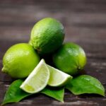 Whole and cut limes sitting on a wooden surface