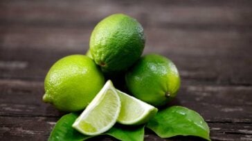 Whole and cut limes sitting on a wooden surface