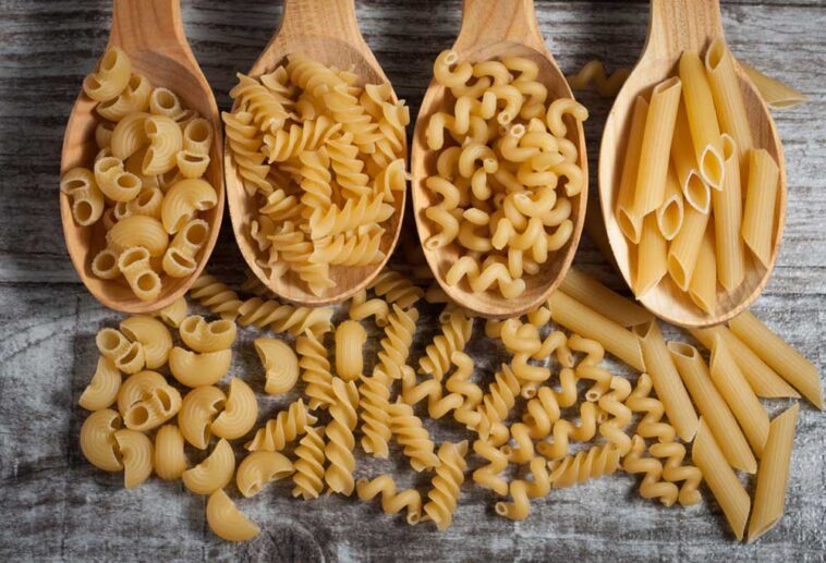 Wooden spoons full of different types of dried pasta