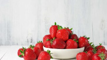 Strawberries spilling from a white bowl onto a white table