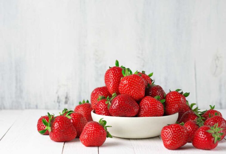 Strawberries spilling from a white bowl onto a white table
