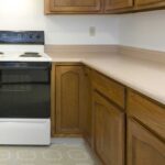 Old kitchen with a white range surrounded by wood cabinets with peach colored counter tops