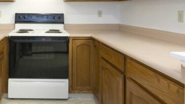Old kitchen with a white range surrounded by wood cabinets with peach colored counter tops