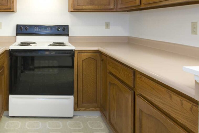 Old kitchen with a white range surrounded by wood cabinets with peach colored counter tops