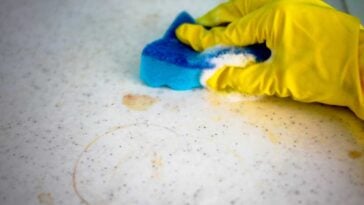 Yellow gloved hand scrubbing stains from a countertop with a blue sponge