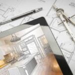 Tablet laying on top of kitchen design plans with drafting tools