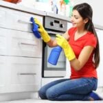 Woman scrubbing kitchen drawers and cabinets with a spray bottle and rag