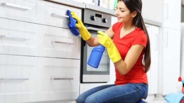 Woman scrubbing kitchen drawers and cabinets with a spray bottle and rag