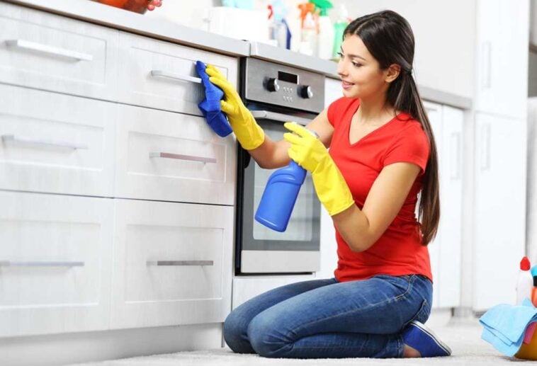 Woman scrubbing kitchen drawers and cabinets with a spray bottle and rag