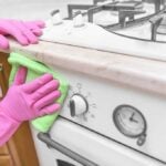 Person wearing pink gloves scrubbing the front of a greasy stove