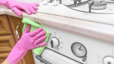 Person wearing pink gloves scrubbing the front of a greasy stove