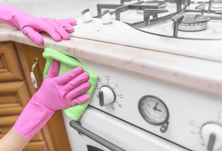 Person wearing pink gloves scrubbing the front of a greasy stove
