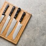 4 knives with black handles laying on a cutting board on a countertop