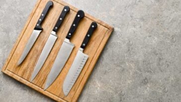 4 knives with black handles laying on a cutting board on a countertop