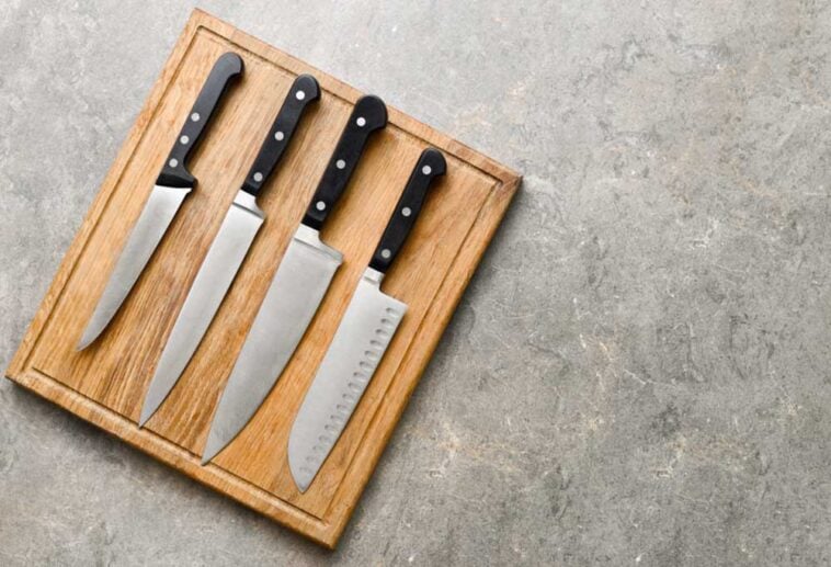 4 knives with black handles laying on a cutting board on a countertop