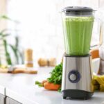 Blender full of green smoothie surrounded by fruit