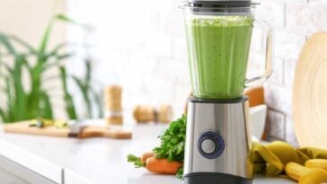 Blender full of green smoothie surrounded by fruit