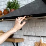Persons hand extended upward to turn on a black range hood