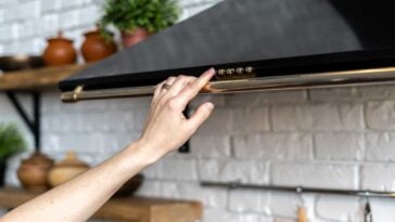 Persons hand extended upward to turn on a black range hood