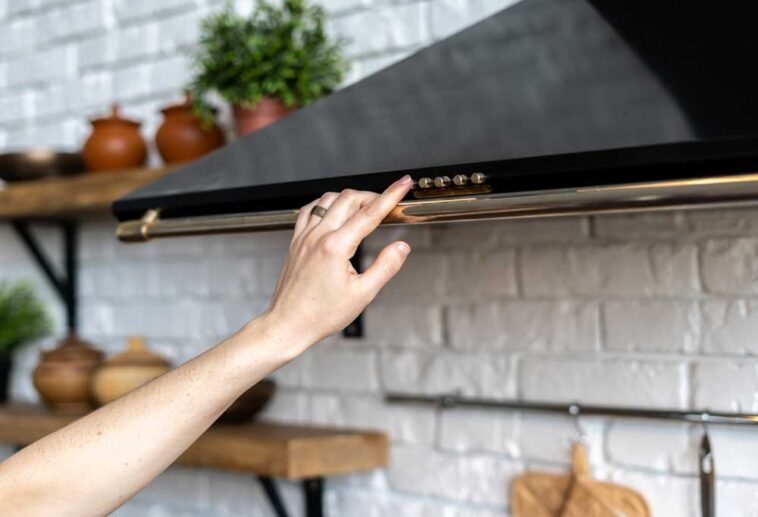 Persons hand extended upward to turn on a black range hood