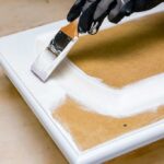 Hand holding a paint brush, painting a cabinet door white